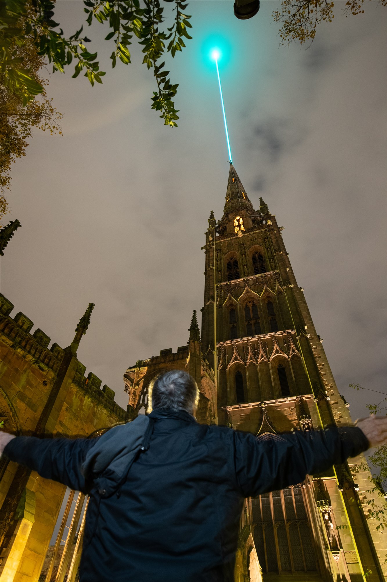 A cyan laser beam extending above a lit Coventry tower