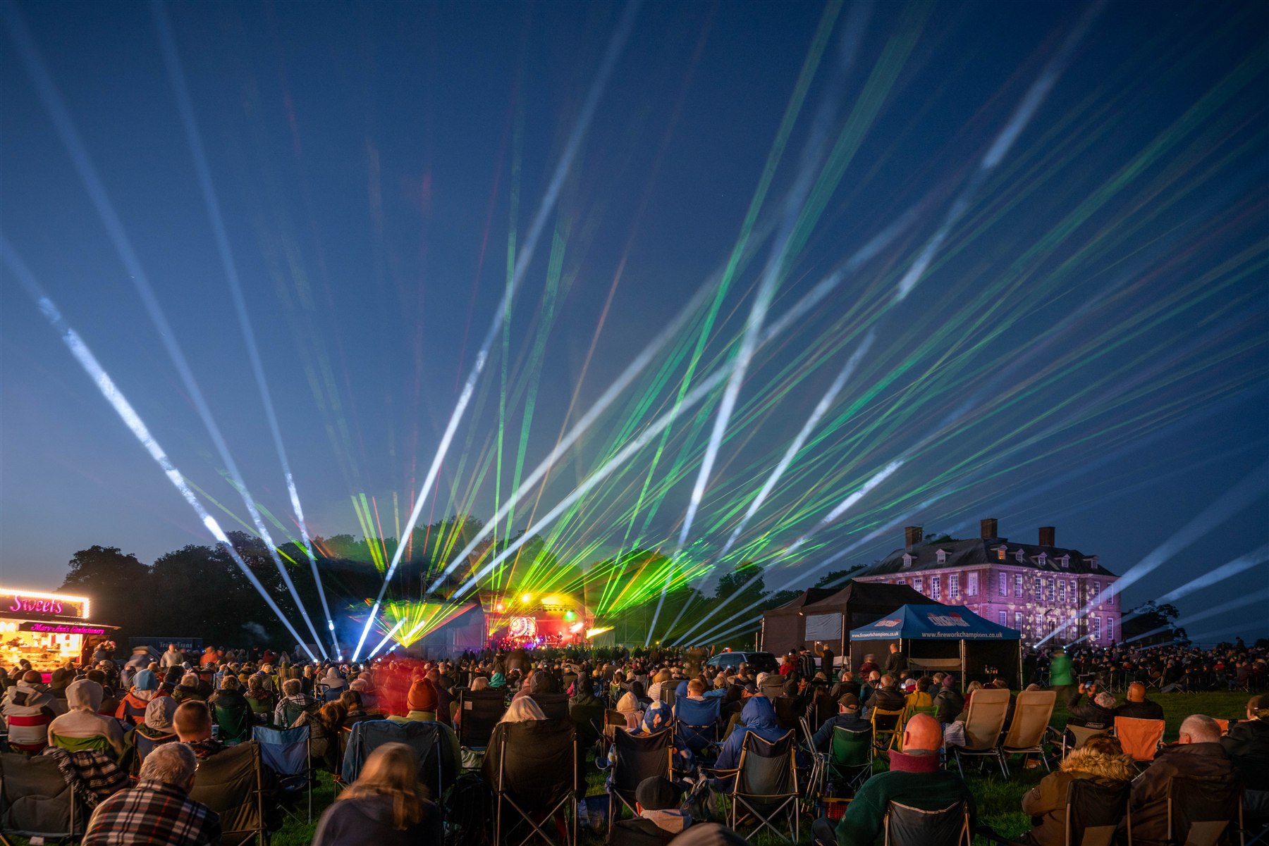 Green laser beams and white lighting above an outdoor concert audience