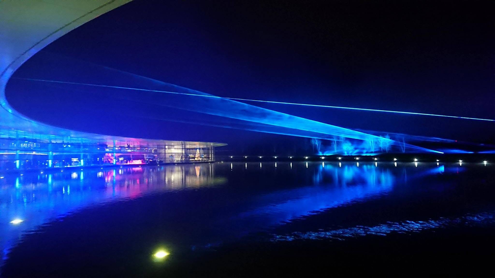 Blue laser beams sweep across a waterfront at night